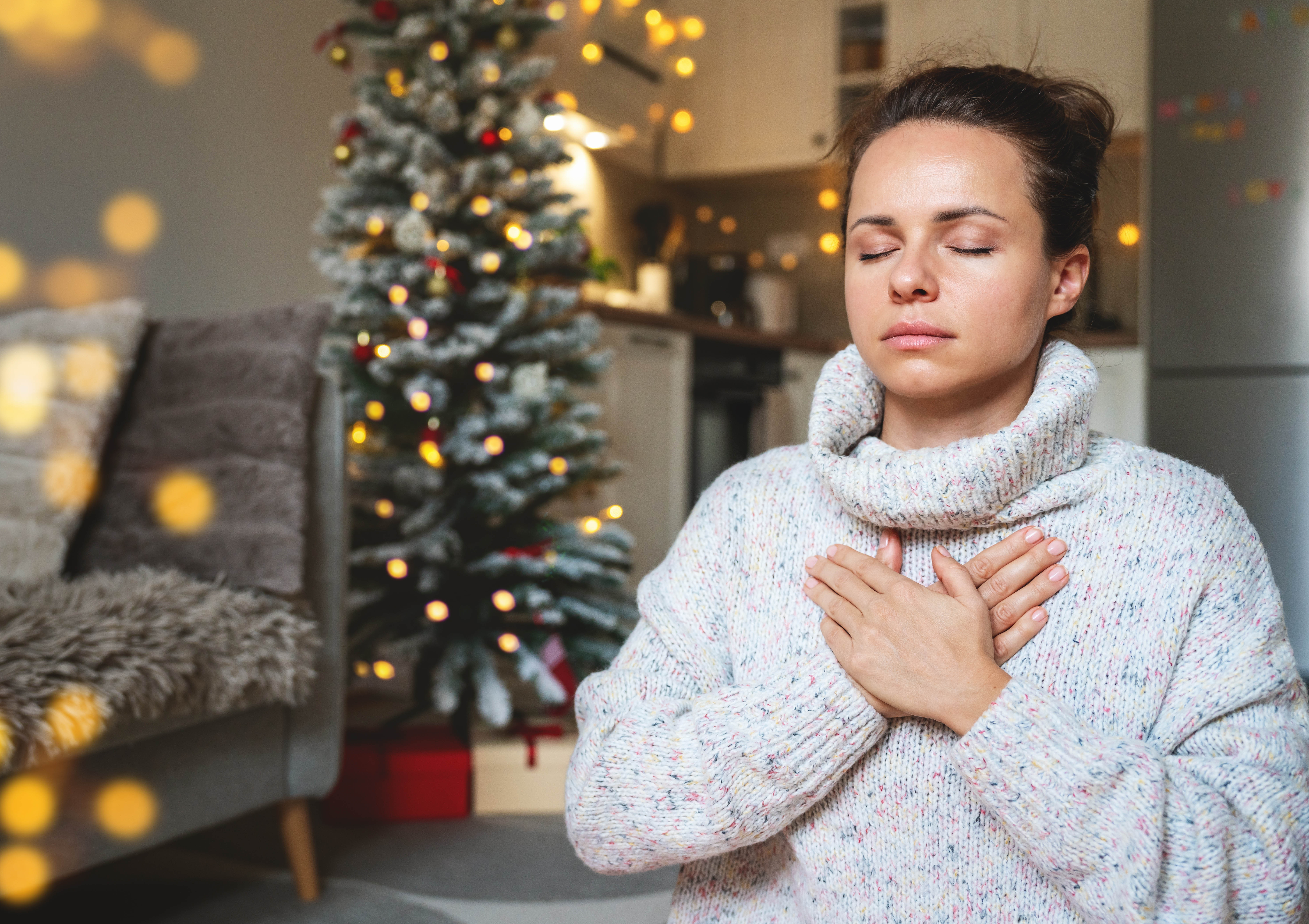 Woman sitting with hands over her heart, taking deep, calming breaths in front of the Christmas tree